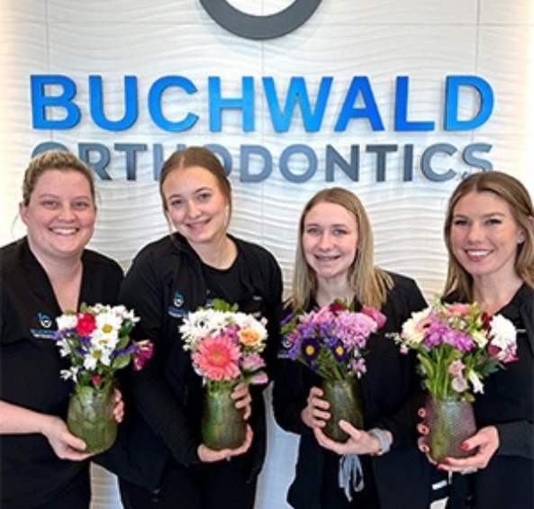 Four smiling orthodontic team members each holding vase with flowers