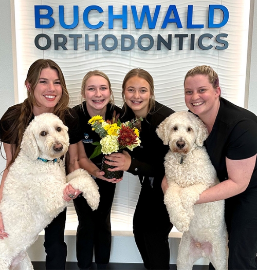 Buchwald Orthodontics team smiling with vase of flowers and two white dogs