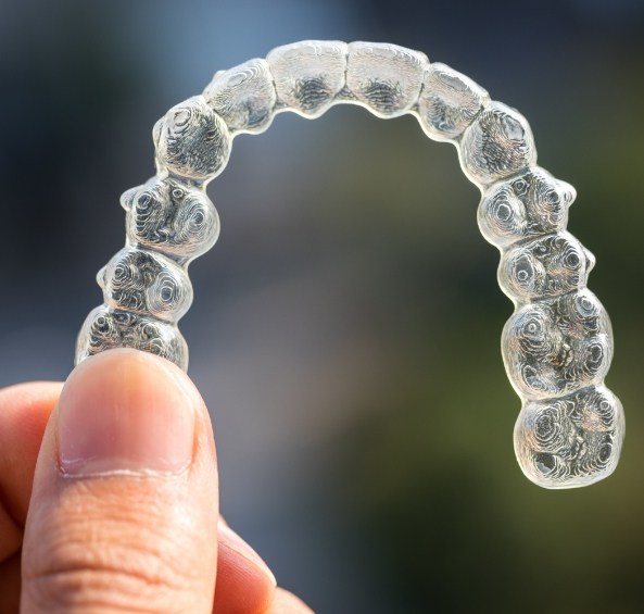 Hand holding a clear aligner for Invisalign treatment in Prosper