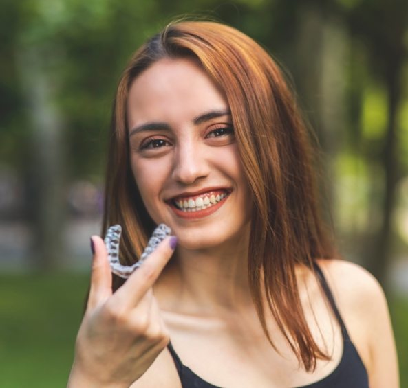 Smiling young woman holding Invisalign aligner outdoors
