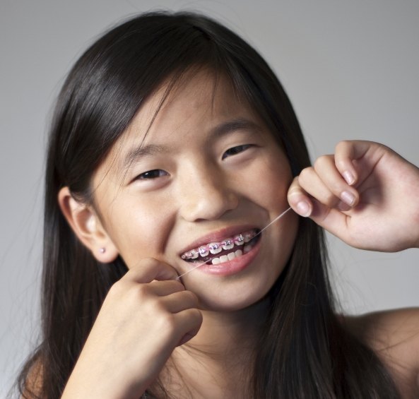 Young girl with metal braces flossing her teeth