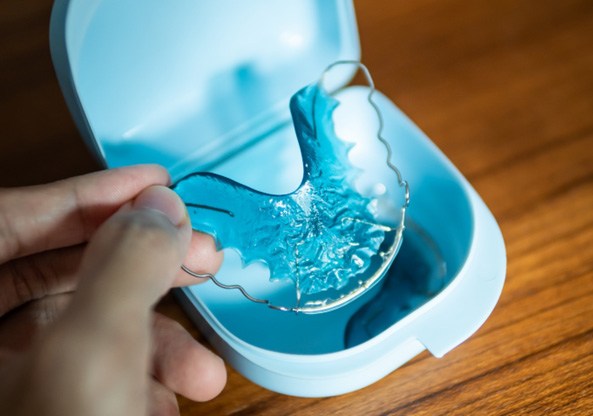 Blue orthodontic retainer in Prosper being held above it’s case on a wooden table