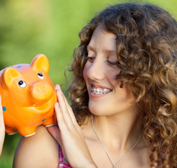 Woman with braces in Prosper smiling at an orange piggy bank